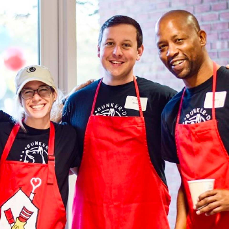 Three volunteers in red RMHC aprons, posing during service at a House program