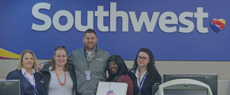 Shaded background image, five people from Southwest Airlines standing in front of the Southwest sign at the airport