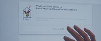 Shaded background image, close-up of someone at a McDonald's kiosk opting in to "Round up" to donate to RMHC