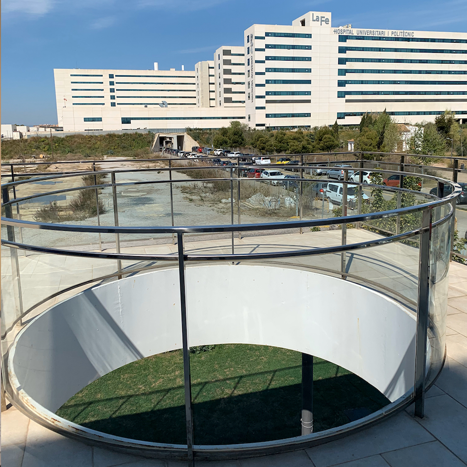 Circular opening in outdoor modern deck with glass and metal handrail panels. Buildings are in the background.