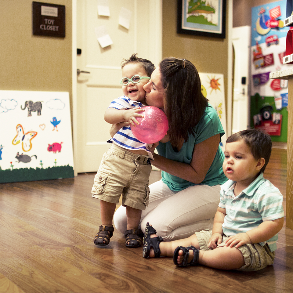 An RMHC family enjoying time together in a common area; mother with children, hugging one son holding a balloon as another sits