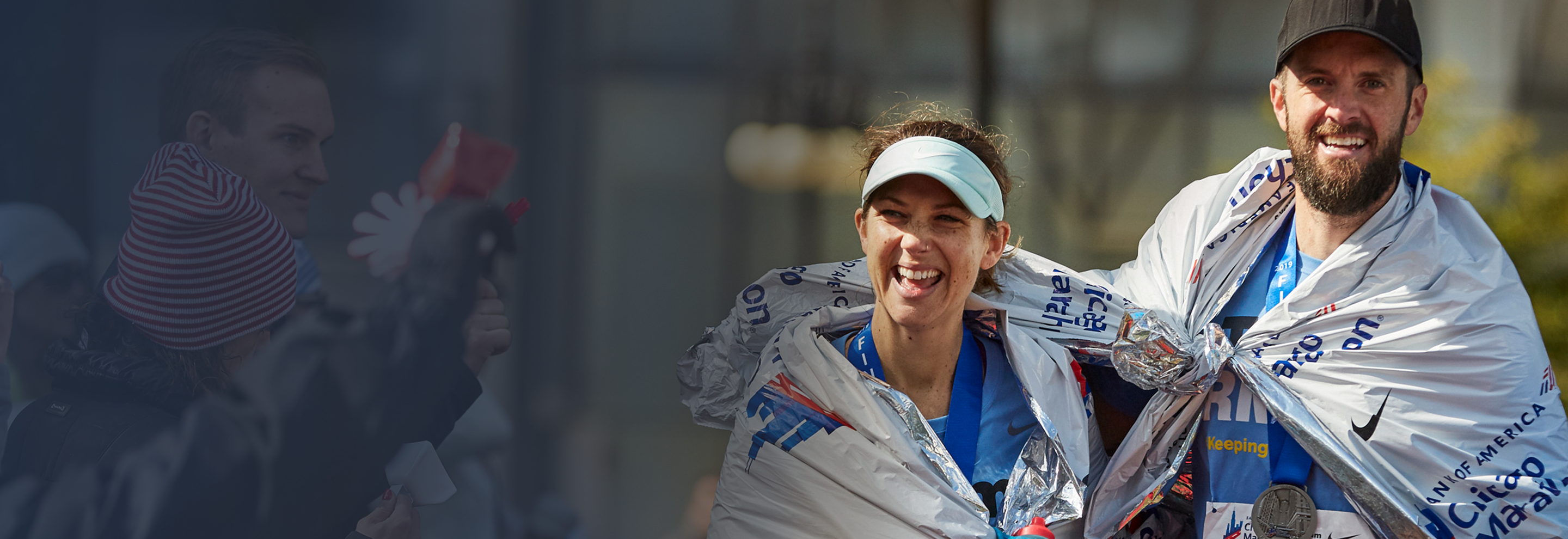 Team RMHC marathoners, a man in a black hat, right, and a woman in a teal visor, center, wrapped in space blankets, spectators cheering in soft focus on far left, at the Bank of America Chicago Marathon