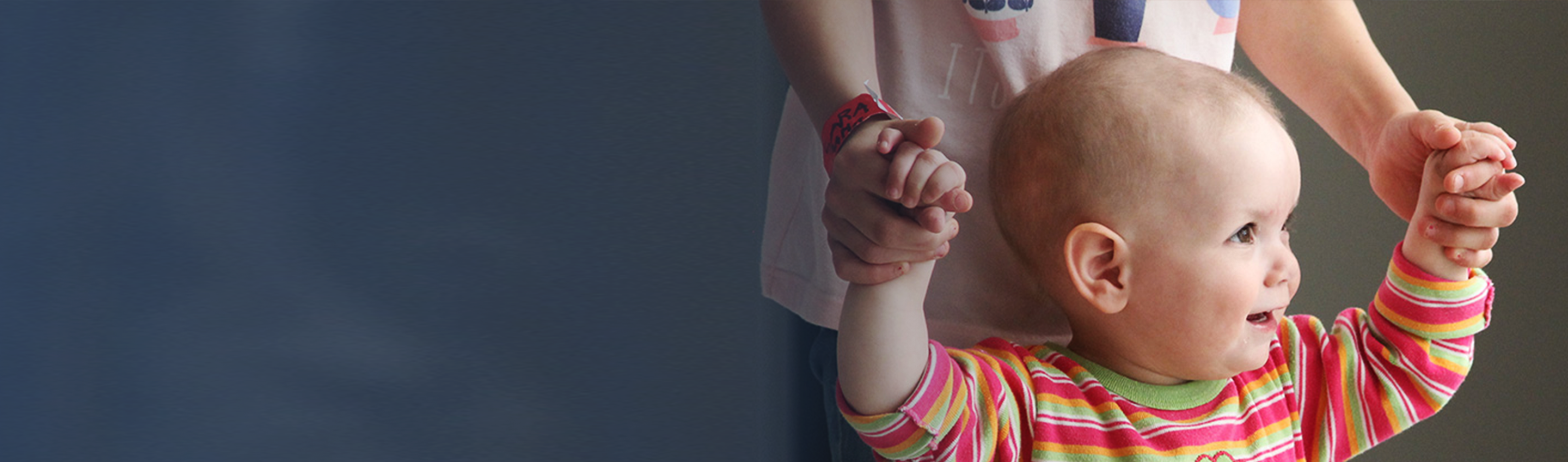 Smiling toddler walking with hands raised and holding those of an adult, RMHC Uruguay